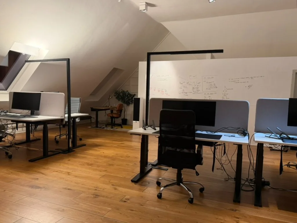 Arbeitsraum unter dem Dach mit Schreibtischen, Stehleuchten und Whiteboard