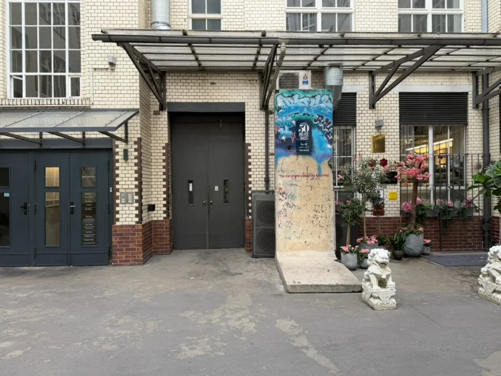 Hofeingang mit Seitenaufgang, einem Segment der Berliner Mauer und zwei Steinlöwen